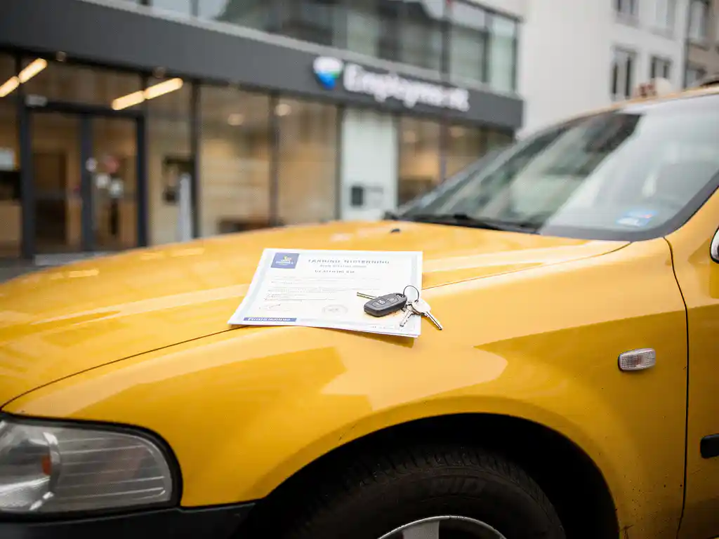 Gele taxi geparkeerd voor een modern Nederlands uitzendbureau, met opleidingscertificaat en autosleutels op de motorkap.